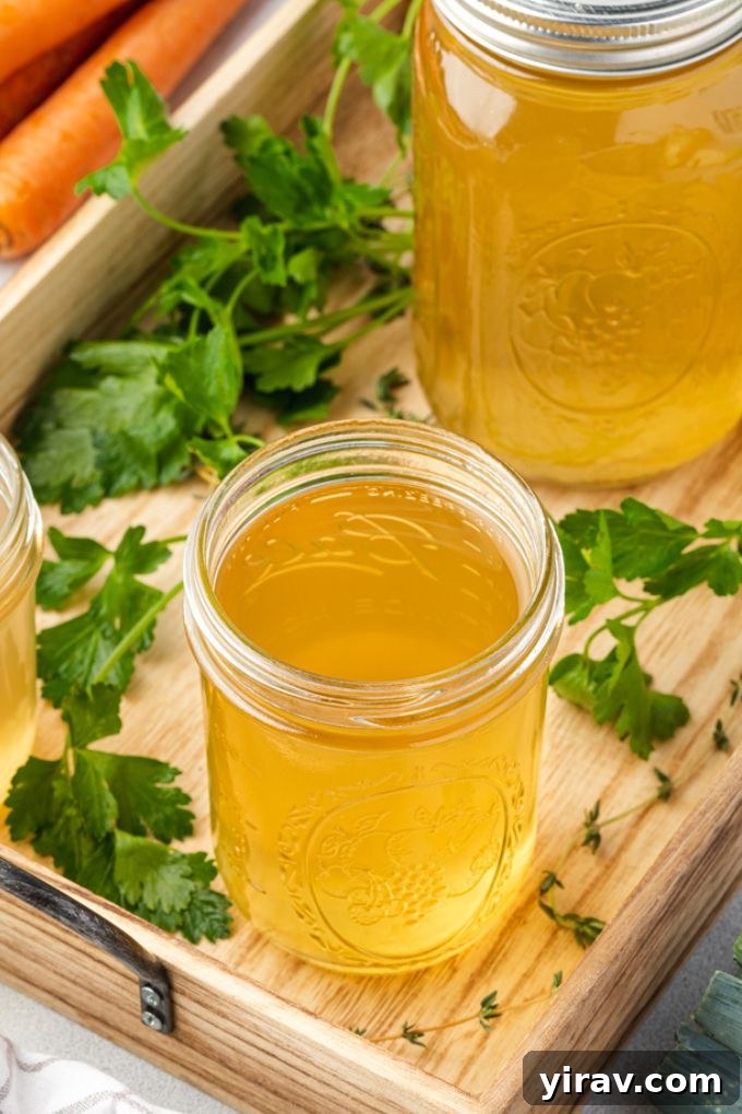 Three glass jars of homemade vegetable stock sitting on a rustic wooden serving tray, garnished with fresh herbs, ready for use or storage.
