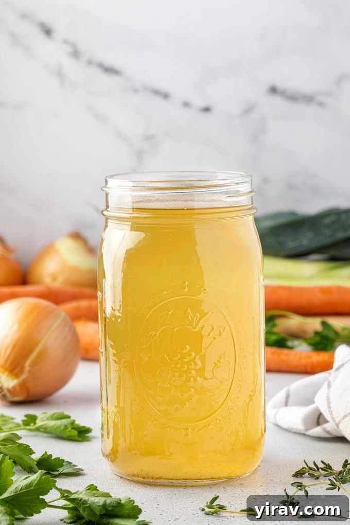 A jar of homemade vegetable broth with fresh vegetables like carrots, celery, and herbs artfully arranged around it on a wooden surface, highlighting the natural ingredients.