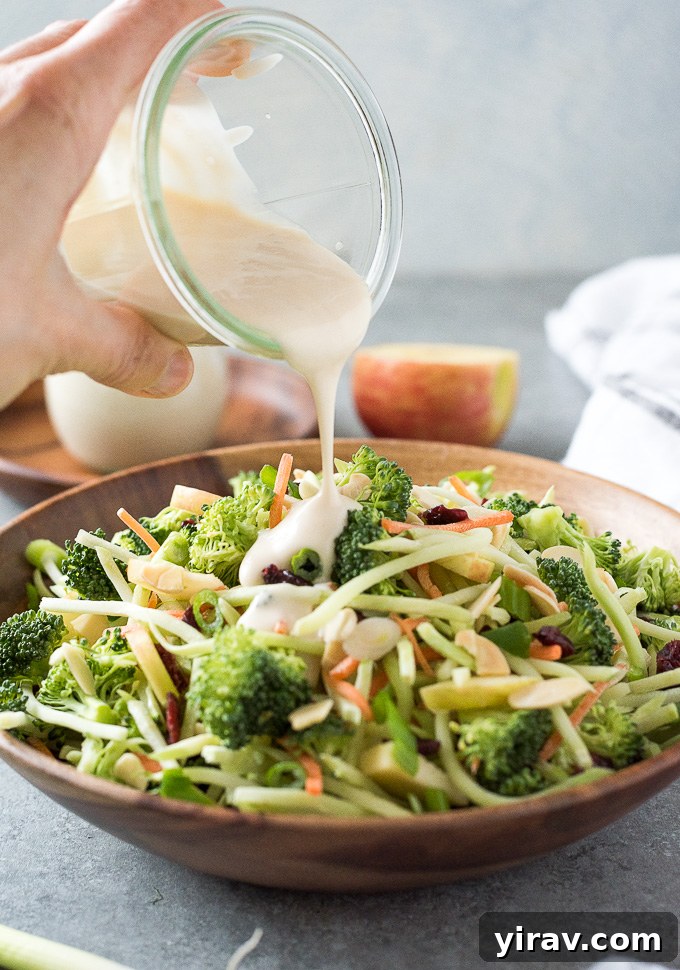 Crisp Broccoli Delight 6 Broccoli Slaw in a bowl with creamy dressing being poured from a jar over the top, highlighting its fresh appeal.