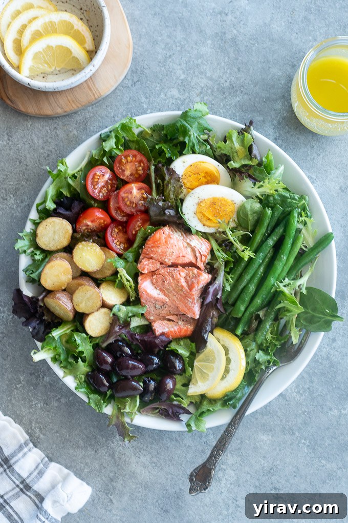 Vibrant Salmon Nicoise 6 A serving of Salmon Niçoise Salad on a white plate, garnished with lemon slices and accompanied by a fork.