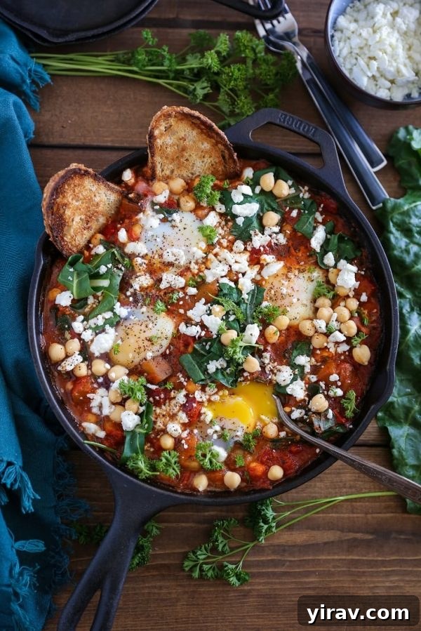 A black bowl of vibrant eggplant shakshuka, generously topped with chickpeas and chard, served with toasted bread slices for dipping.
