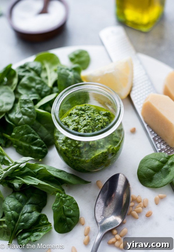 A jar of freshly made pesto sauce, surrounded by vibrant greens, lemon, and parmesan cheese, illustrating the ingredients used.