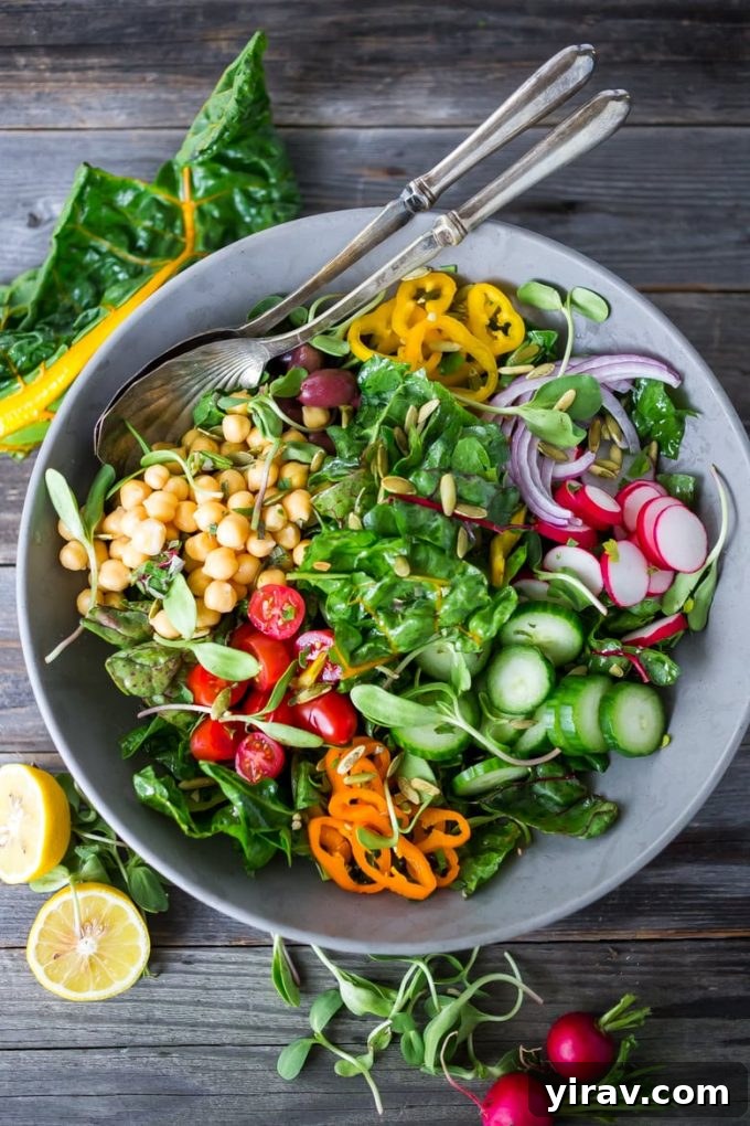 An overhead view of a colorful Mediterranean chard salad in a gray bowl, brimming with fresh ingredients and a zesty dressing.