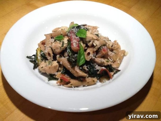 A white plate of delicious pesto chicken pasta with Swiss chard, showing a complete and satisfying one-pot meal.