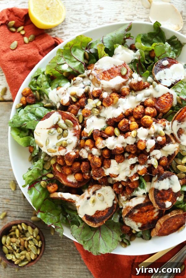 A vibrant roasted sweet potato and chickpea salad with Swiss chard on a white plate, dressed with a creamy tahini dressing.