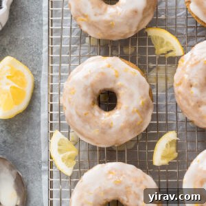A stack of three lemon baked donuts, one of which is glazed, on a white plate with a fork.