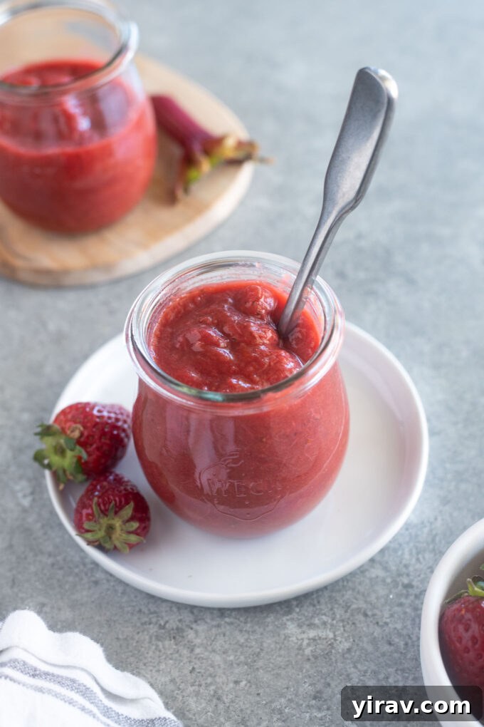 23 Rhubarb Recipes Essential Produce Guide 20 A jar of Small Batch Strawberry Rhubarb Jam with a spoon nestled inside, highlighting its homemade goodness.