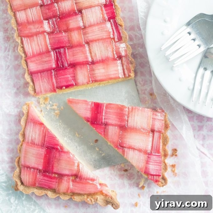 23 Rhubarb Recipes Essential Produce Guide 8 A beautiful sliced rhubarb tart presented next to a white plate with forks, adorned with delicate rhubarb strips.