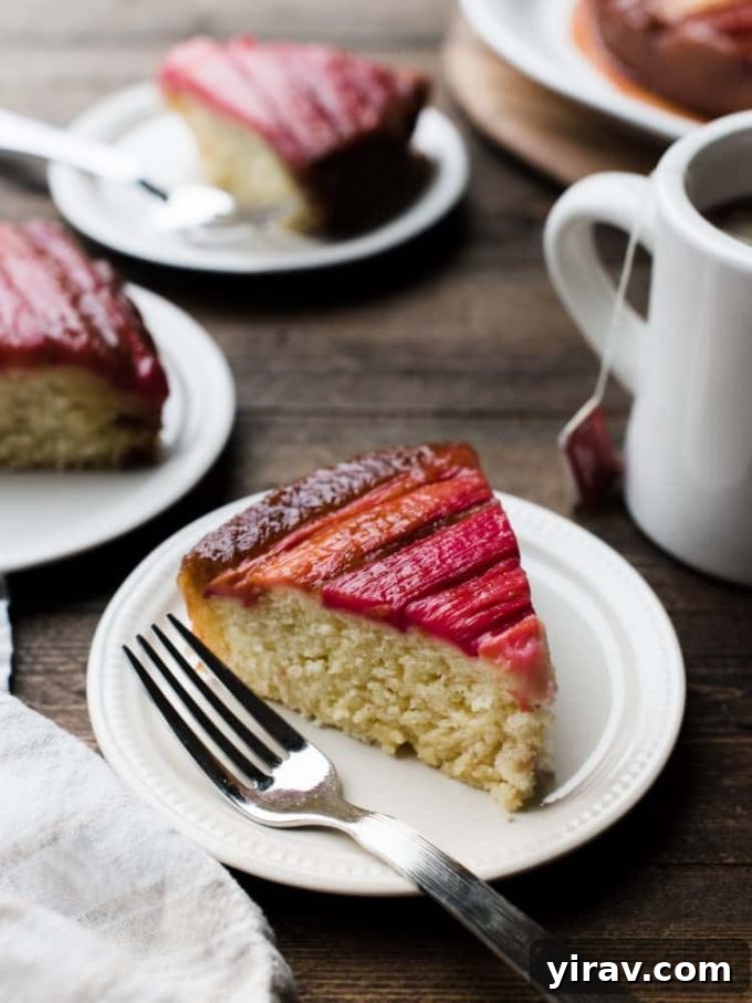 23 Rhubarb Recipes Essential Produce Guide 9 A slice of moist Rhubarb Upside Down Cake on a white plate with a fork, with more slices and a coffee mug in the background.