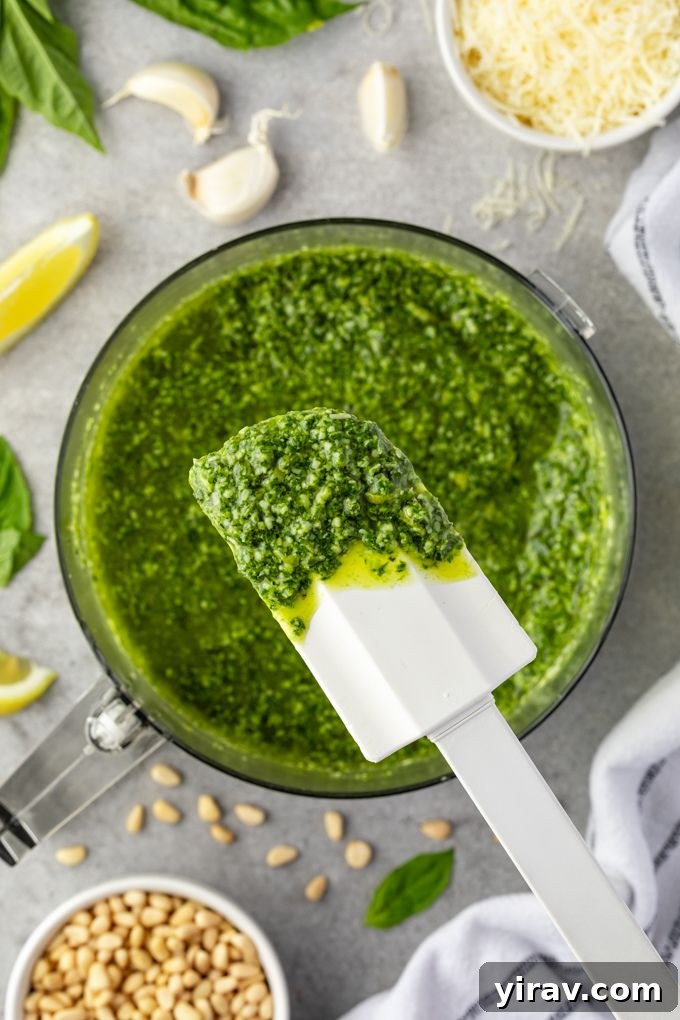 Close-up of fresh basil, garlic, and pine nuts being pulsed in a food processor to make pesto