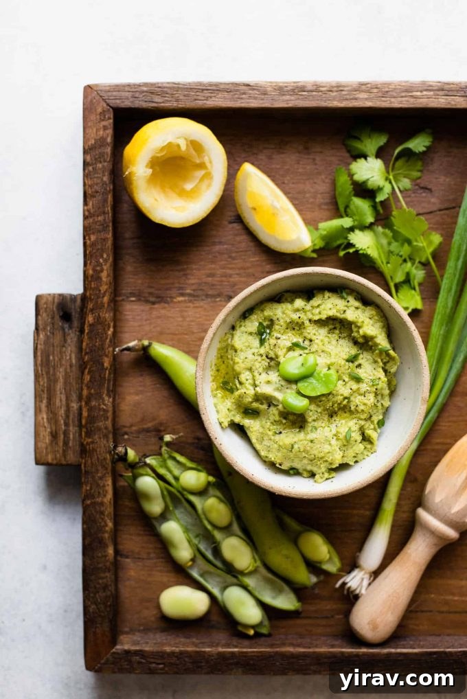 Creamy Fava Bean Dip served in a white bowl on a rustic wooden serving board, perfect for snacking or spreading.