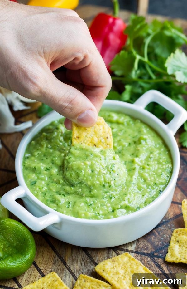 Avocado salsa verde dip in white bowl with chip dipped in