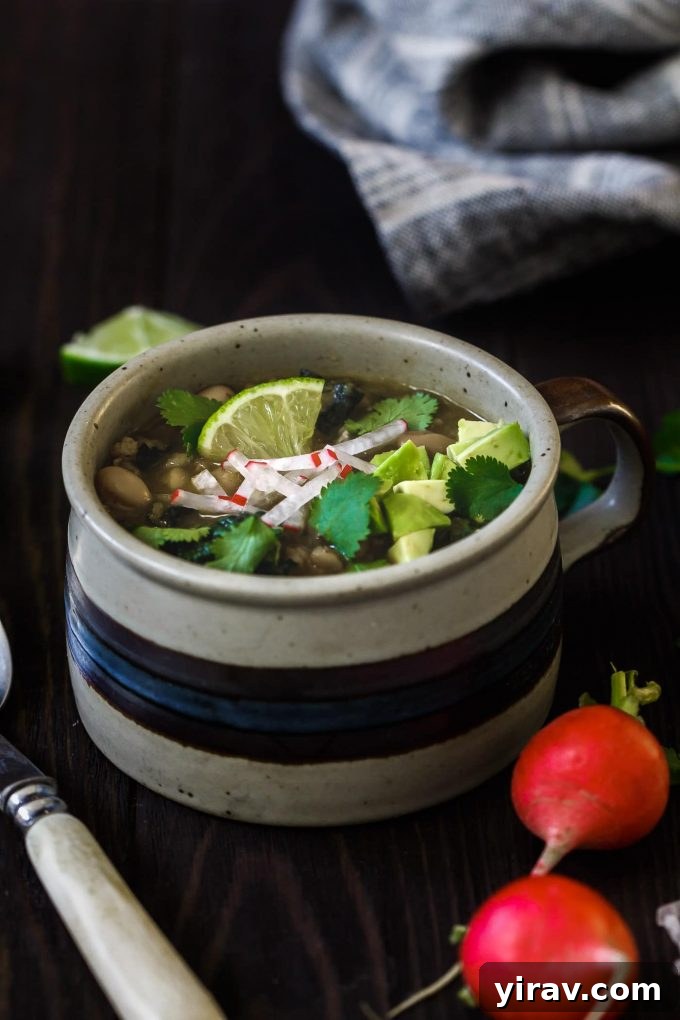 A mug of posole verde garnished with lime and cilantro. Radishes in the foreground.