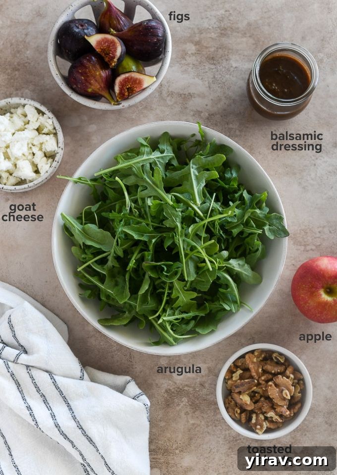 Close-up of all the fresh ingredients laid out for making the arugula fig salad: fresh figs, arugula, goat cheese, apple, and walnuts.