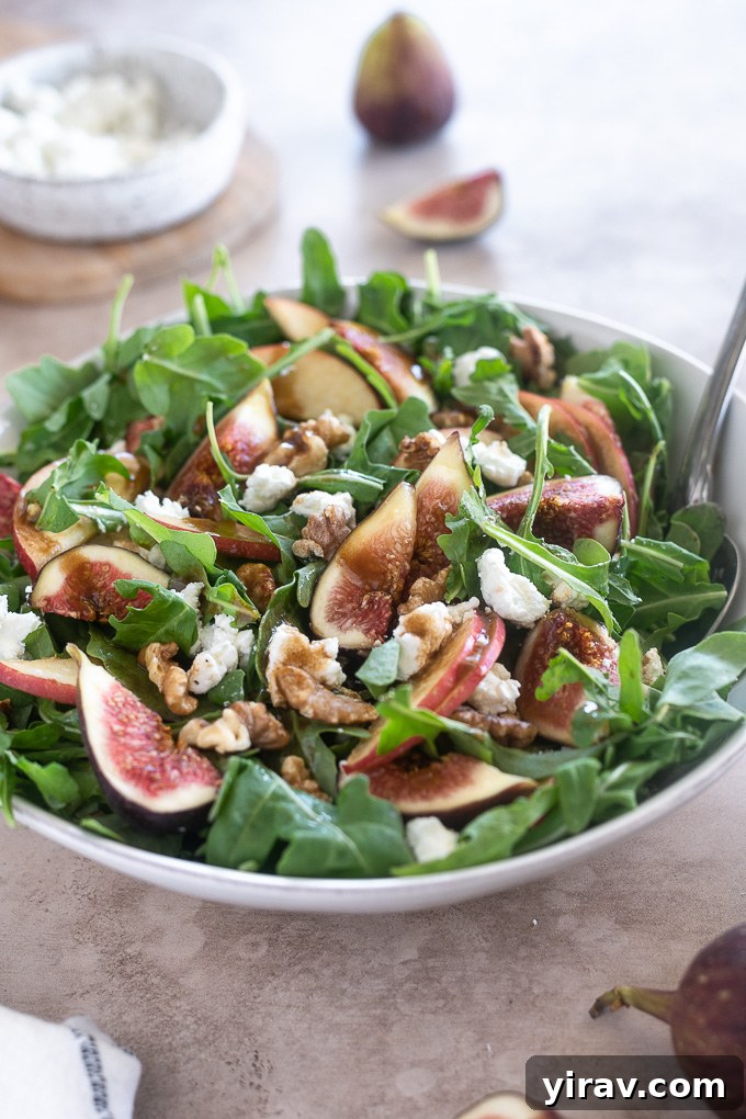 Arugula fig salad in a white bowl, with balsamic dressing generously drizzled over the top, ready to serve.