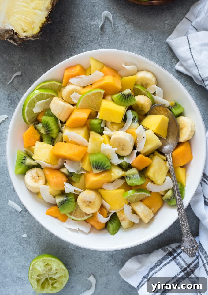 Close-up of tropical fruit salad with lime wedges and coconut flakes.