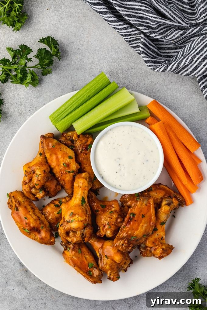 Honey buffalo chicken wings arranged artfully on a platter with fresh celery and carrot sticks, and a side of ranch dip, showcasing an ideal appetizer presentation.