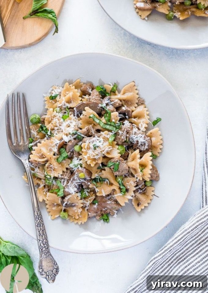 A close-up shot of creamy Italian sausage pasta with bow tie pasta, peas, and mushrooms on a white plate with a fork, ready to be enjoyed.