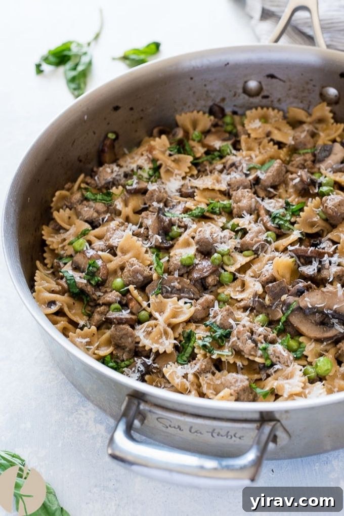 A generous serving of creamy Italian sausage bow tie pasta with visible pieces of sausage, mushrooms, and peas, served directly from a large skillet, highlighting its one-pot convenience.