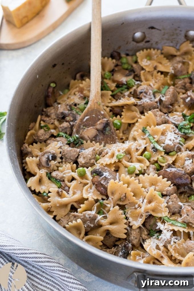 A wooden spoon scooping a portion of Italian sausage bow tie pasta from a large skillet, showcasing its creamy texture and the mix of ingredients.