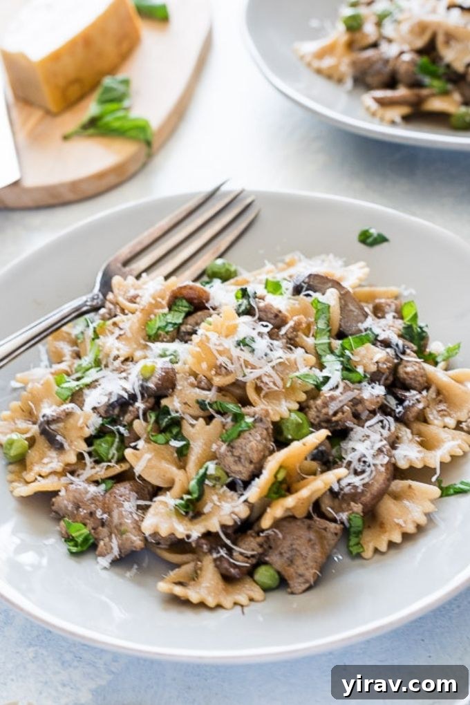 A close-up of a plate of Italian sausage bow tie pasta, generously topped with freshly grated Parmesan cheese and a sprig of fresh basil, emphasizing its delicious appeal.