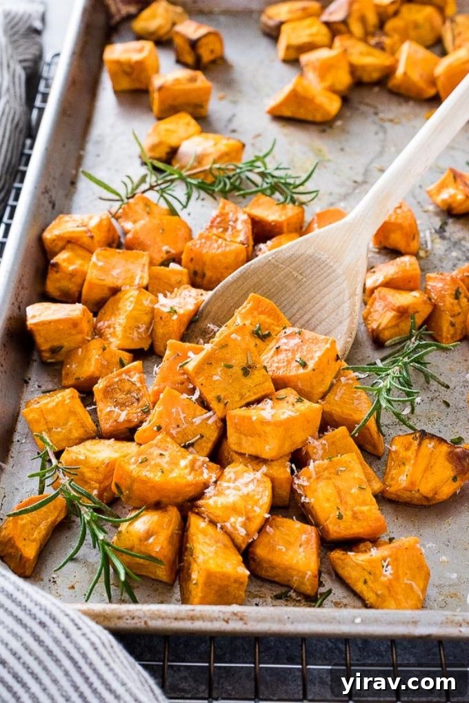 A wooden spoon lifting roasted sweet potatoes from a baking sheet, showing their golden brown exterior.