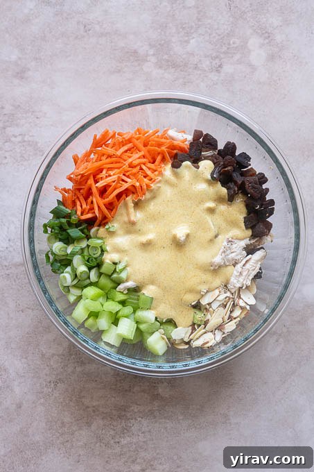 Creamy curry dressing being poured over the chicken salad ingredients in a large bowl before mixing.