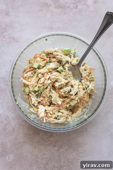 Finished curry chicken salad, perfectly mixed and ready to serve, in a mixing bowl with a serving spoon.