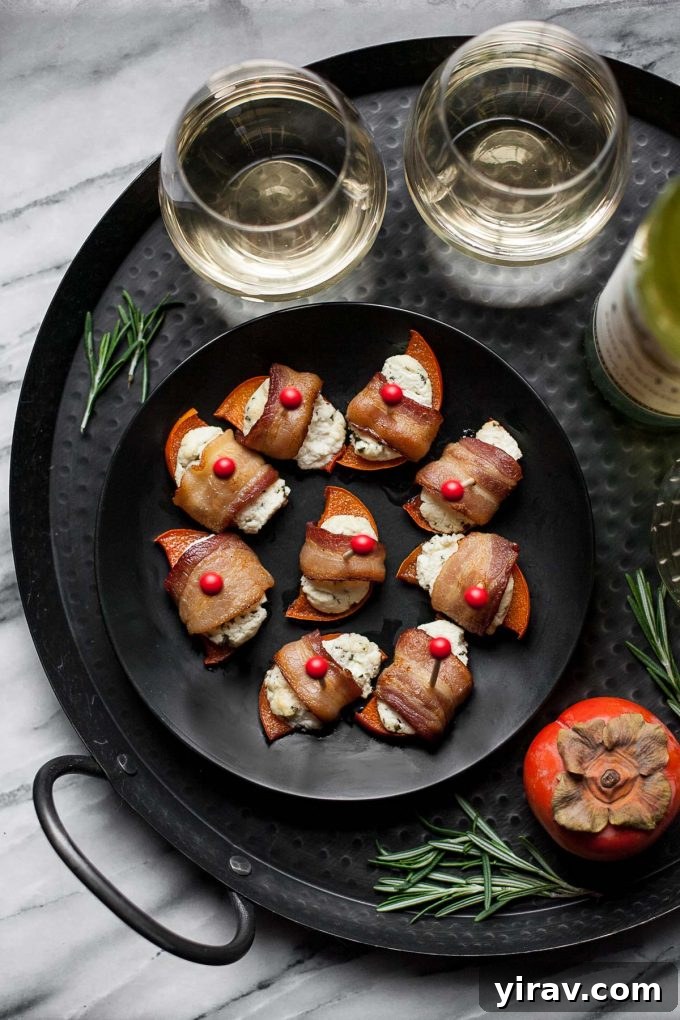 An overhead view of elegant persimmon bacon bites with rosemary goat cheese on a gray plate, accompanied by two glasses of wine.