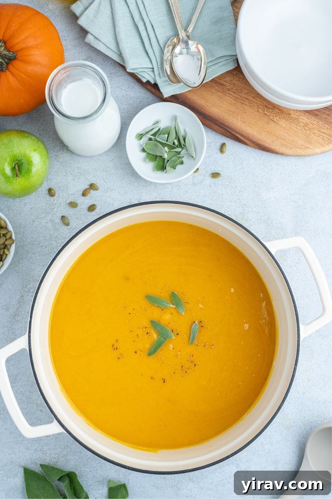 A pot of creamy roasted pumpkin apple soup, garnished with fresh sage leaves.