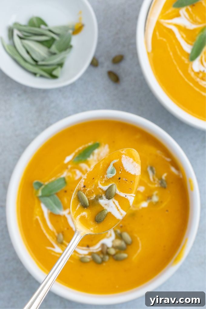 A spoonful of roasted pumpkin apple soup gracefully lifted over a bowl, highlighting its smooth texture and rich color.
