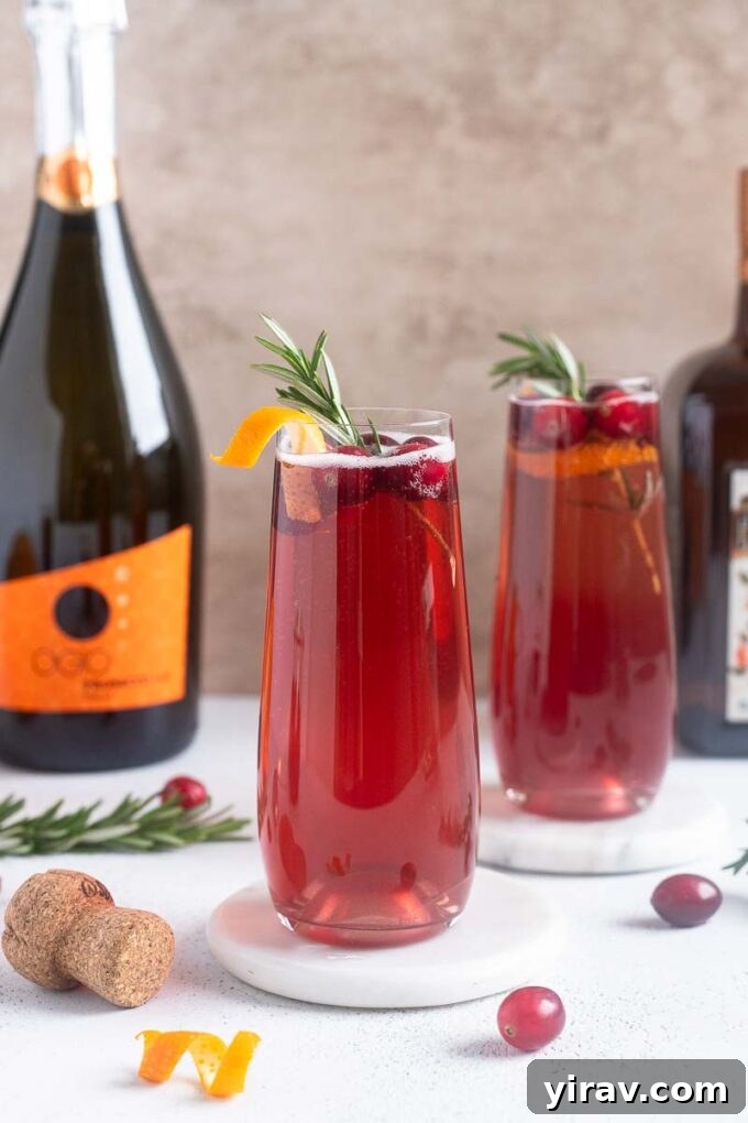 Elegant Poinsettia Cocktails, garnished with fresh cranberries and an orange twist.