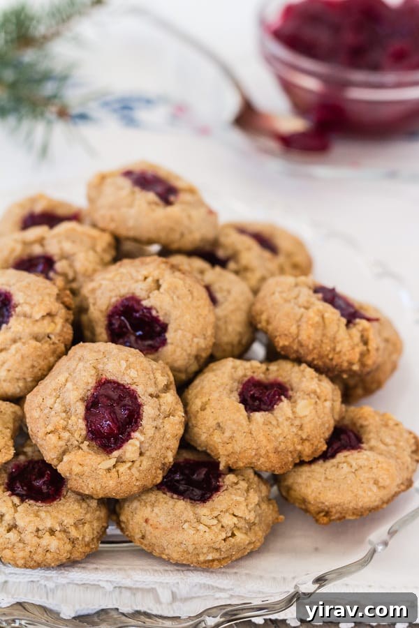 A plate piled high with delicate almond thumbprint cookies, each with a jammy center.