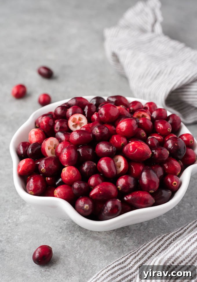 A white bowl brimming with fresh cranberries, some cut in half to reveal their inner texture.