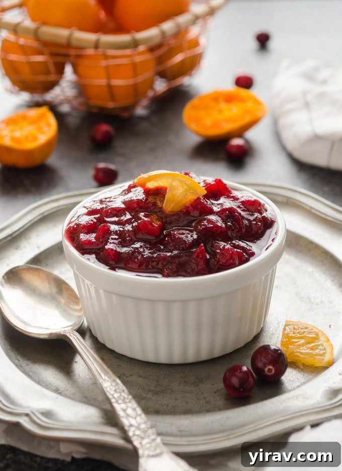 A small ramekin filled with a rich, vibrant cranberry orange sauce, garnished with a twisted orange peel.
