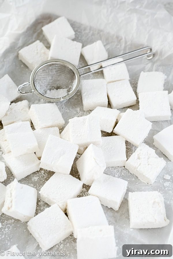 Homemade marshmallows on a baking sheet with powdered sugar and sieve