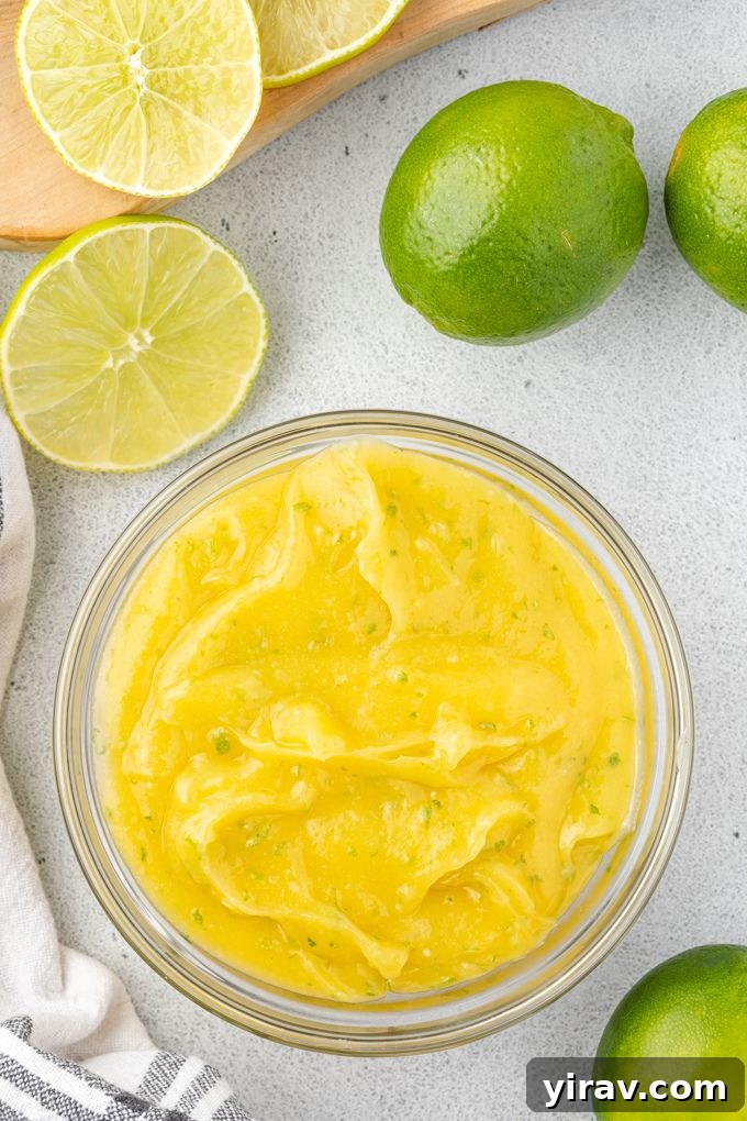 Homemade Lime Curd in a glass bowl surrounded by fresh limes, showcasing its vibrant color.