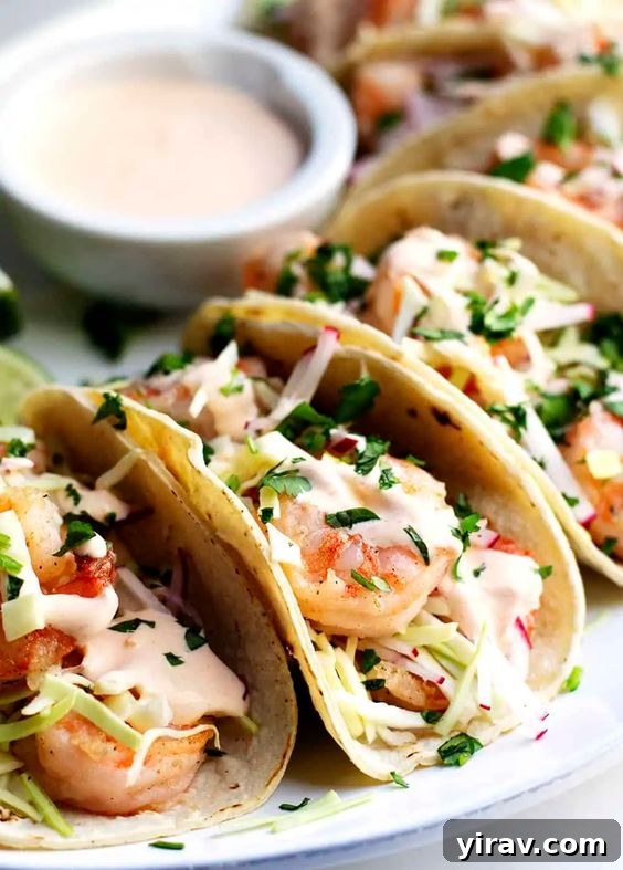 A plate of spicy shrimp tacos with a dish of sauce, perfectly garnished.