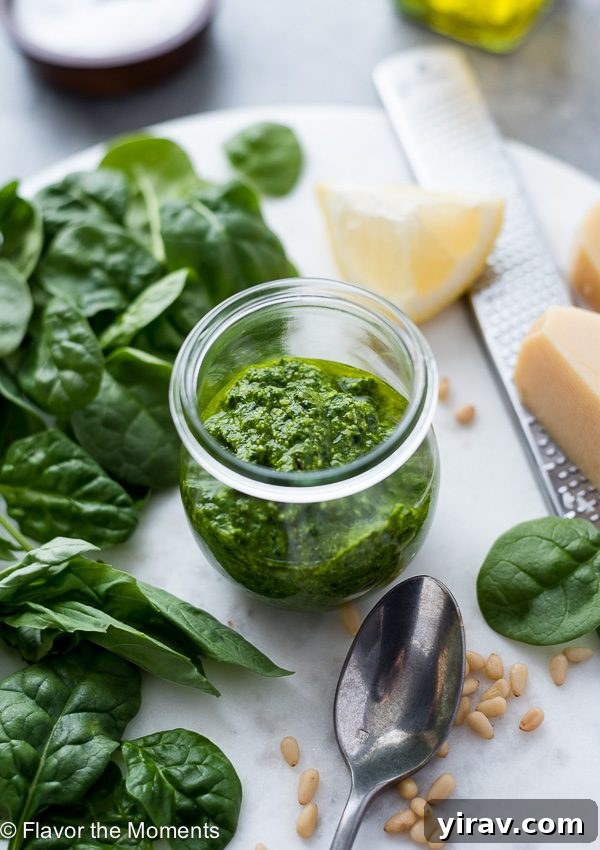 Homemade pesto sauce in a jar next to fresh greens, illustrating the freshness of the ingredients.