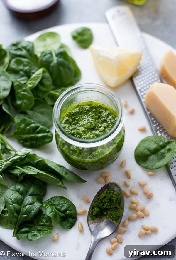 Homemade pesto sauce in a jar, accompanied by fresh spinach, pine nuts, and a wedge of Parmesan, showcasing key ingredients.