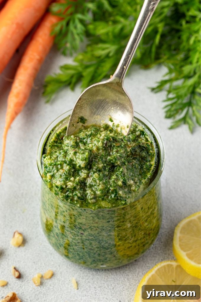 Vibrant Carrot Greens Pesto 7 A spoon scooping creamy, green carrot top pesto from a glass jar, highlighting its luscious texture.