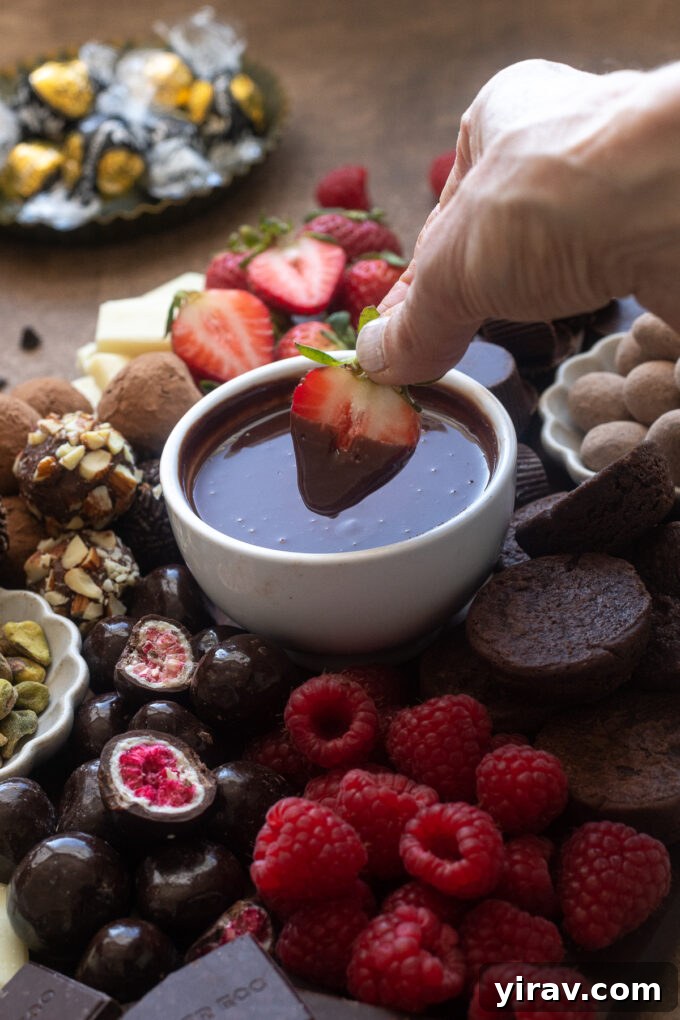 A close-up of a fresh strawberry being dipped into rich chocolate ganache, part of a decadent chocolate dessert board.