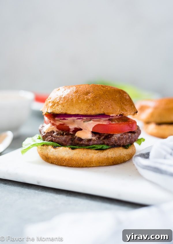 Grilling Burgers Like a Pro 3 A mouthwatering homemade grilled burger, bursting with juices and fresh toppings, served on a white plate.