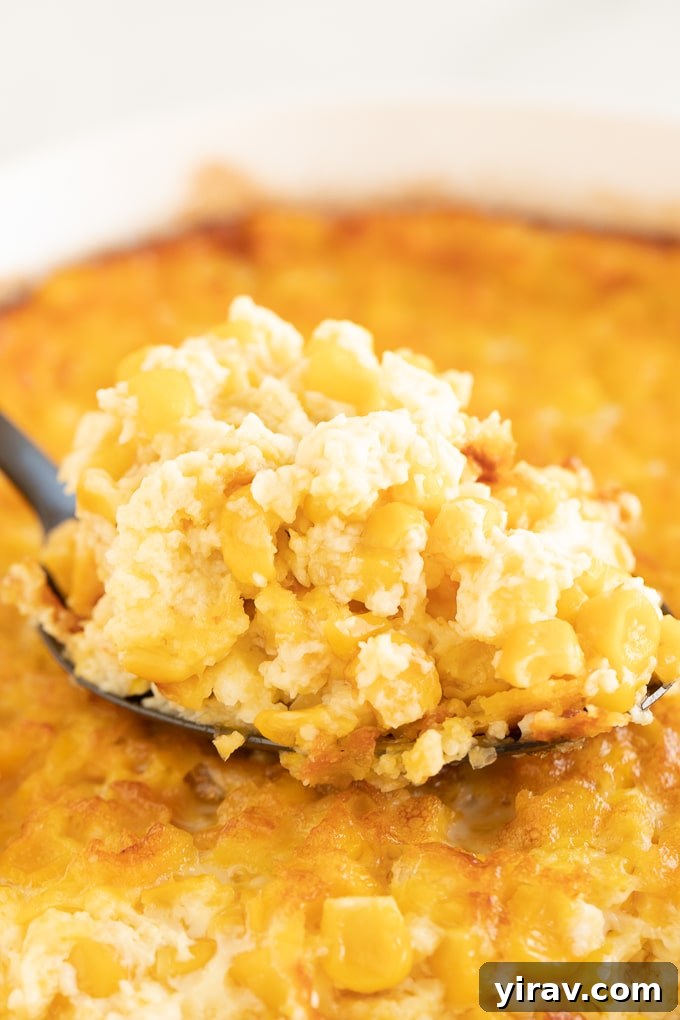 A spoon digging into a creamy, golden Corn Pudding, showcasing its rich texture and inviting warmth.