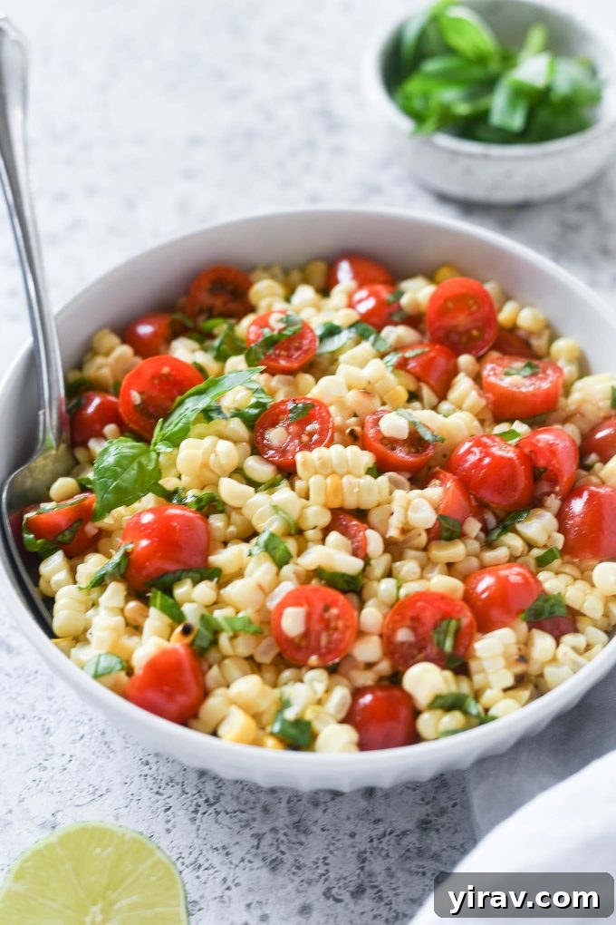 A spoon nestled into a vibrant bowl of Fresh Corn and Tomato Salad, showcasing its colorful ingredients.
