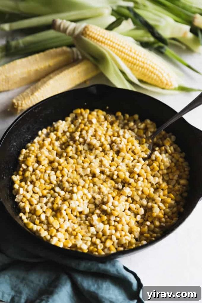 A cast iron skillet filled with Southern Fried Corn, next to fresh ears of corn, evoking a rustic charm.