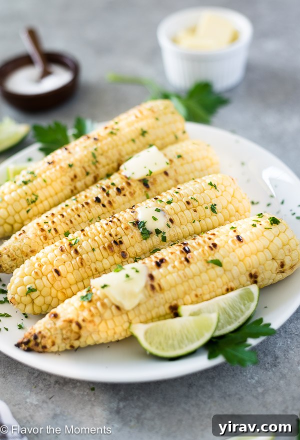 Close-up front view of perfectly grilled corn on the cob, glistening with butter and served with fresh lime wedges.