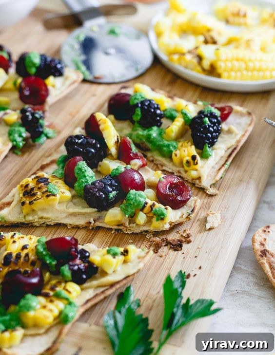 A wooden serving board featuring sliced Hummus Flatbread with Grilled Corn and Berries, elegantly presented.