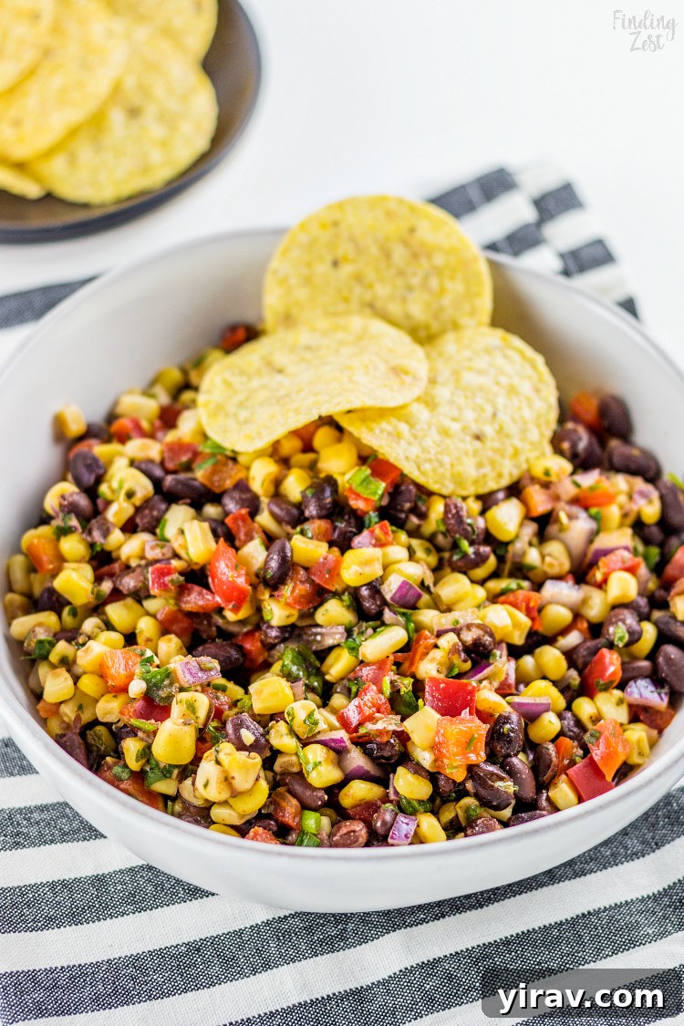 A vibrant bowl of black bean and corn salsa with three crisp tortilla chips, ready for dipping.