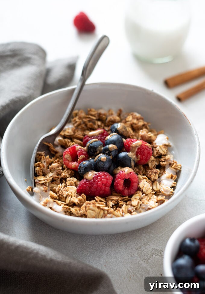 Almond butter granola in a bowl with berries and almond butter drizzle, highlighting the crunchy clusters.